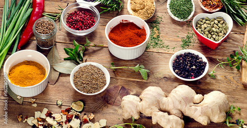 Colorful spices and fresh herbs on a wooden background.