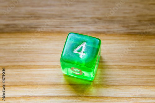 Fototapeta Naklejka Na Ścianę i Meble -  A translucent green six sided playing dice on a wooden background with number four on a top