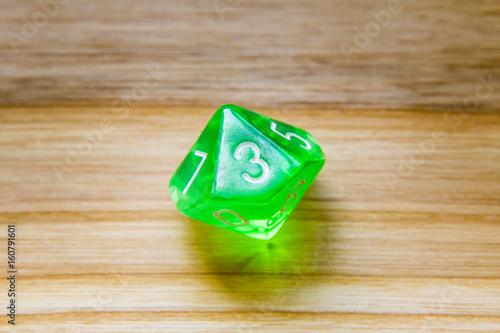 A translucent green ten sided playing dice on a wooden background with number three on a top photo