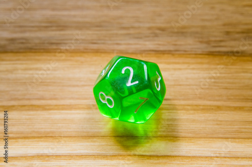 A translucent green twelve sided playing dice on a wooden background with number two on a top photo