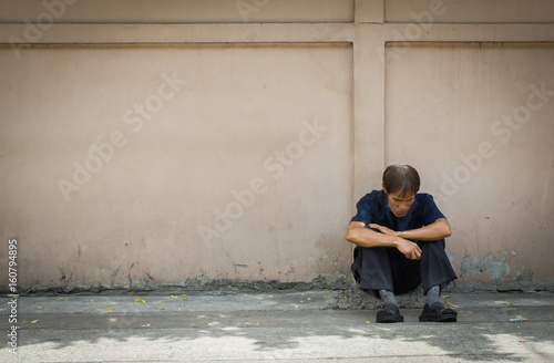 Old man sitting on the old concrete floor with concrete wall for background.