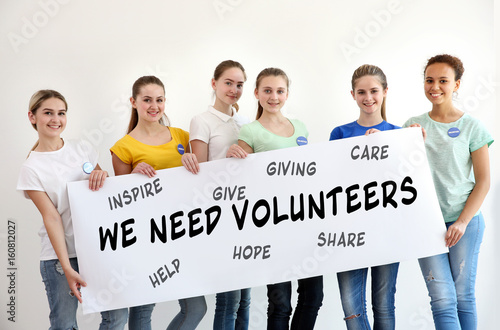 Group of teens holding poster with text WE NEED VOLUNTEERS on color background