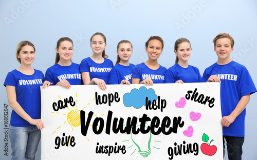 Group of teens holding poster with word VOLUNTEER on color background
