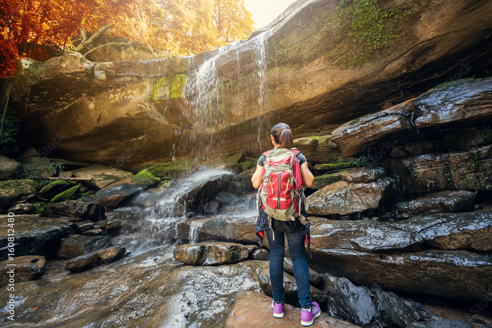 Hiking. Hikers woman with a backpack looking at a waterfall in the forest.