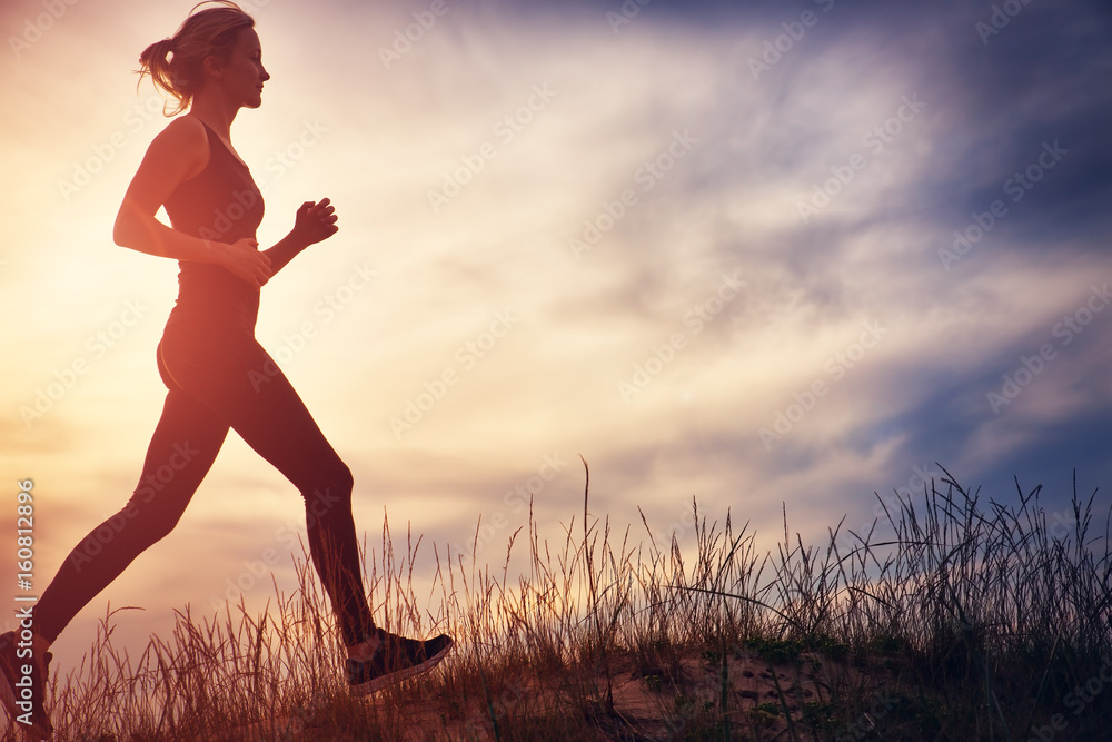 Young woman running on the field near seaside at sunset. Active person outdoors at the dusk in summer Young woman running on the field near seaside at sunset. Active person outdoors at the dusk in summer