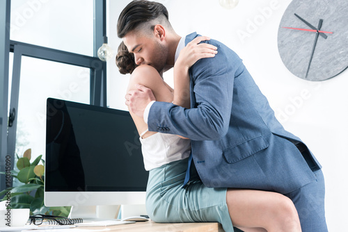 young passionate business colleagues kissing in foreplay at workplace in office
