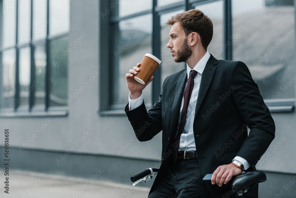 Stylish young businessman sitting on bicycle and drinking coffee Stylish young businessman sitting on bicycle and drinking coffee