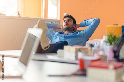 caucasian business person sitting in office thinking daydreaming hands behind head.