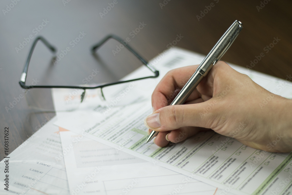 Close up of a man's hand holding pen and filling out business documents and forms Close up of a man's hand holding pen and filling out business documents and forms