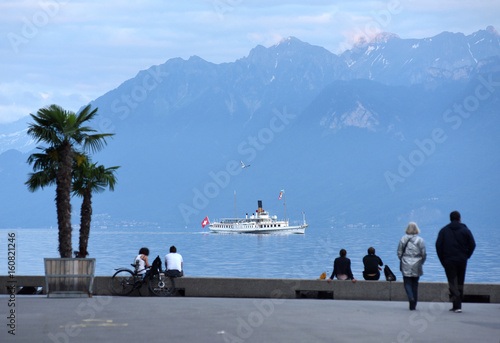 People at the embankment on Lake Geneva in Lausanne with Cruise boat and mountains on the background.