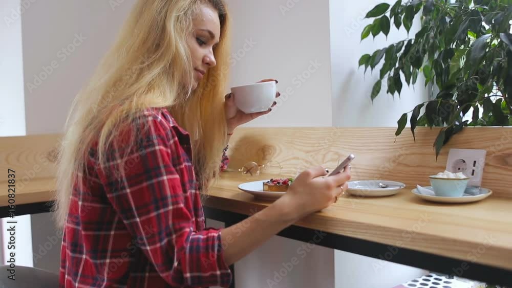 Student girl using app on phone drinking coffee smiling in cafe Student girl using app on phone drinking coffee smiling in cafe