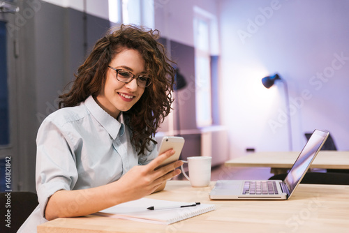 Curly girl wearing glasses smiling while looking at her phone