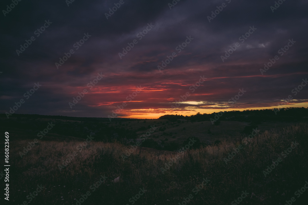 Sun sets over the tops of forest trees in clouds. Panoramic photo of purple, orange and dark clouds in the sky illuminated by the setting sun