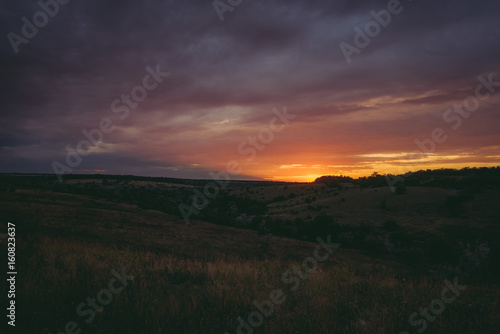 Sun sets over the tops of forest trees in clouds. Panoramic photo of purple, orange and dark clouds in the sky illuminated by the setting sun photo