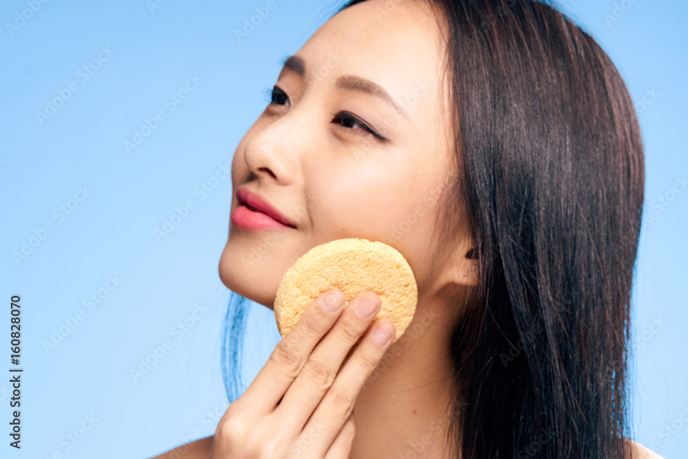 Woman rubs her face with a sponge, a woman looks after a face, a woman on a blue background portrait Woman rubs her face with a sponge, a woman looks after a face, a woman on a blue background portrait