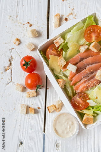Caesar salad with fish in box on wooden surface
