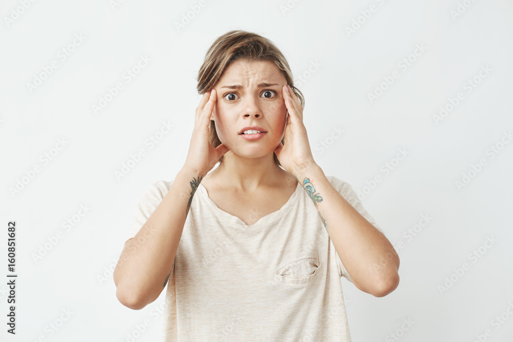 Young beautiful girl ashamed looking at camera frowning with fingers on temples over white background. 