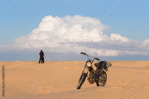 Men and woman with motorcycle in the desert against a cloudy sky background