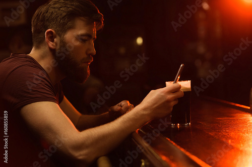 Young bearded man using mobile phone while having beer