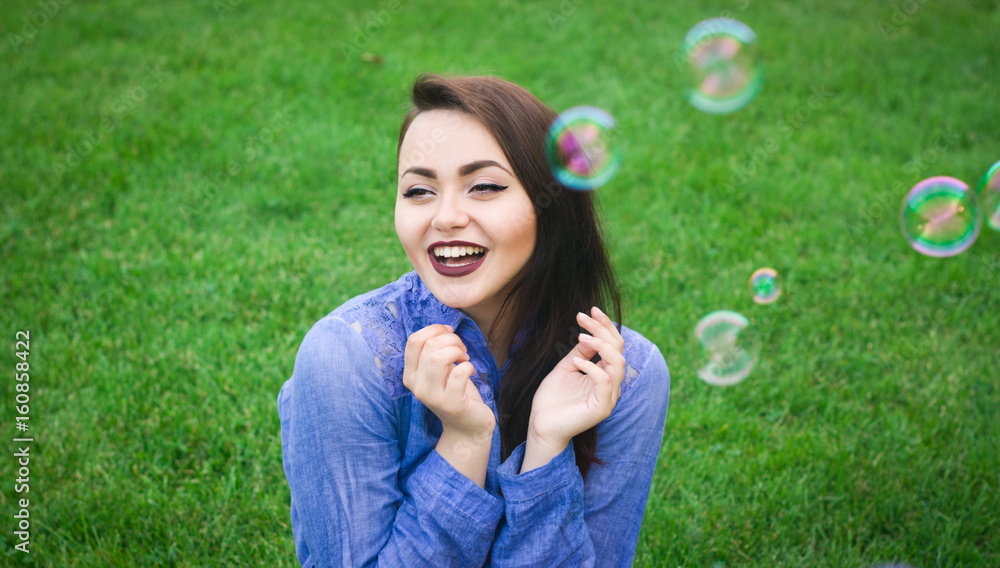 Happy young girl sitting on green grass with soap bubbles Happy young girl sitting on green grass with soap bubbles
