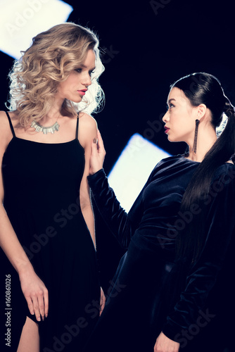 Two sensual glamour multiethnic women spending time in black evening dresses at event