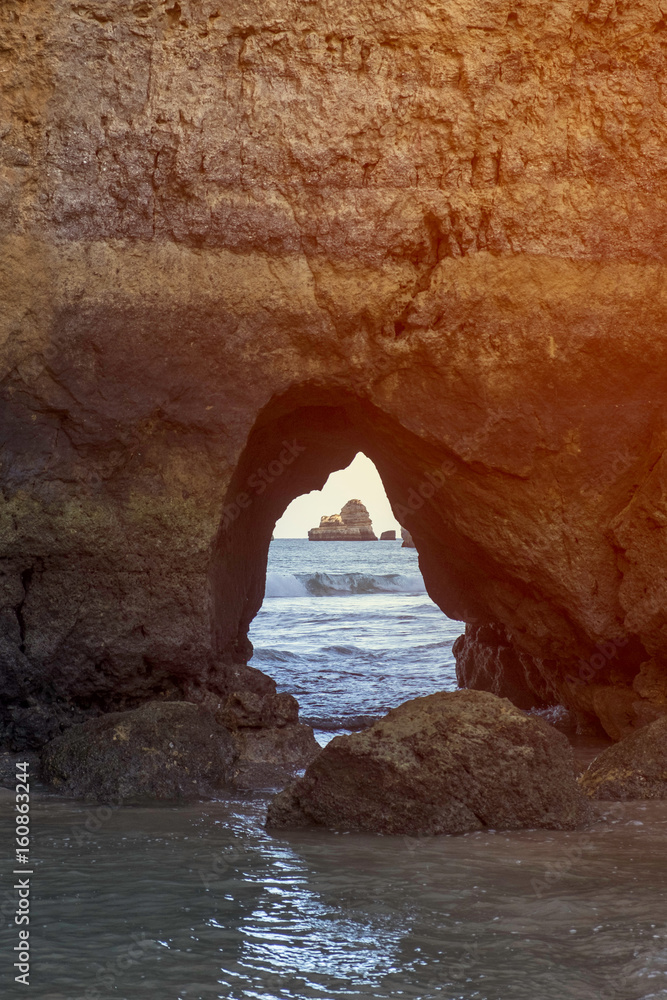 A distant stone boulder matching up with the shape of a stone archway on the beach in Lagos, Portugal 