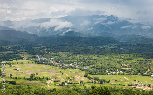 Panorama view of green land with sunlight and mountain covered by cloud and fog in countryside of Thailand on rainy season.