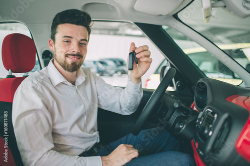 Hand holding car key remote, with modern car backgrounds. man sitting inside new car with keys.