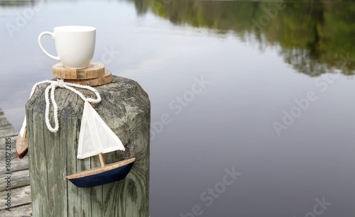 White cup by the dock with wooden sail boat