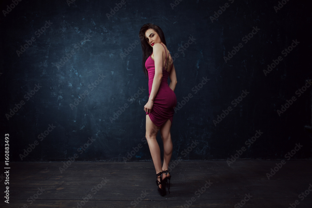 Glamorous stylish fashion model in a red dress posing stands on dark background. Fall fashion. Vogue Style. Glamorous stylish fashion model in a red dress posing stands on dark background. Fall fashion. Vogue Style.