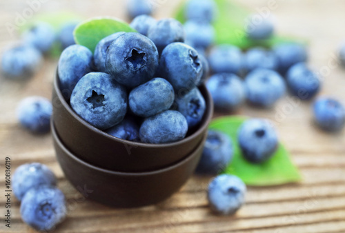 Bowl of fresh ripe sweet juicy blueberries with leaves on wooden background