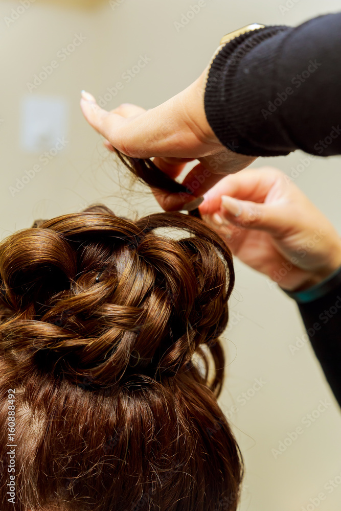 Fototapeta premium Woman hairdresser making hairstyle using curling iron for long hair of young female