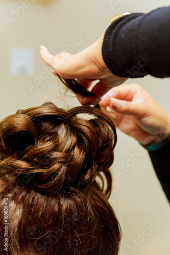 Woman hairdresser making hairstyle using curling iron for long hair of young female