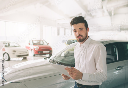 friendly vehicle salesman presenting new cars at showroom. Photo of young male consultant showing new car in auto show. Concept for car rental © estradaanton