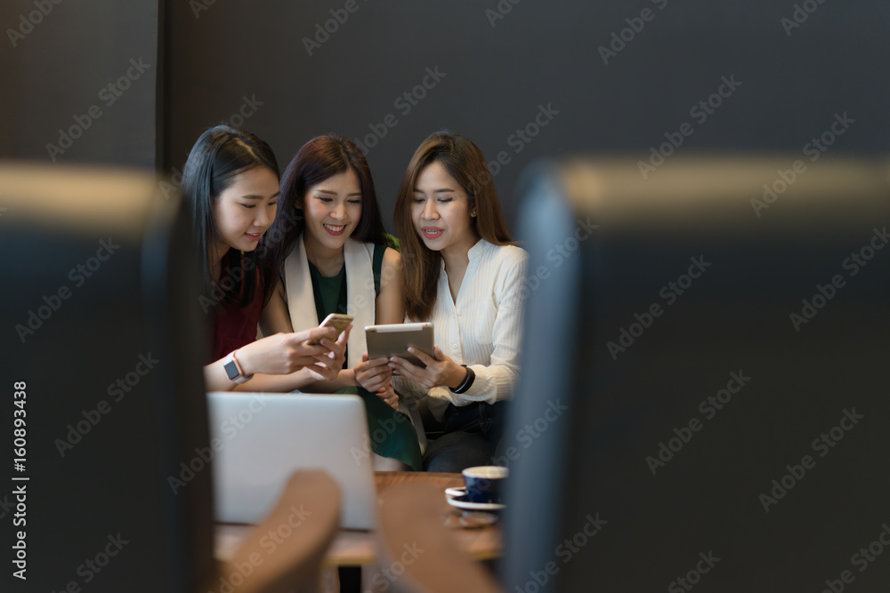 Three beautiful Asian girls using smartphone and laptop, chatting on sofa at cafe, modern lifestyle with gadget technology or working woman on casual business meeting outside office concept.