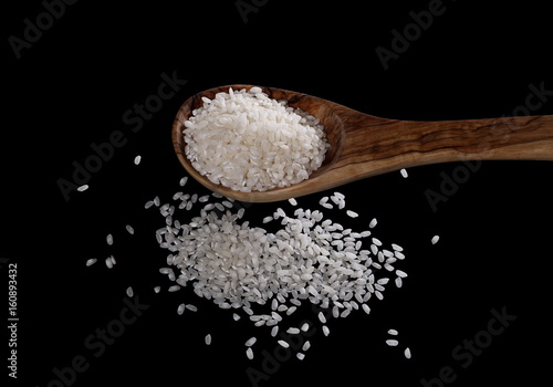 White rice in a wooden spoon isolated on black background