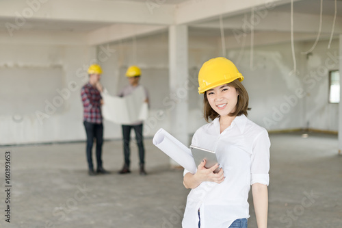 Portrait of smiling young architect or handsome engineer holding rolled up blueprints with building construction background. photo