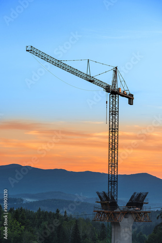Crane in the forest on the background of mountains. Building new road in mountains.