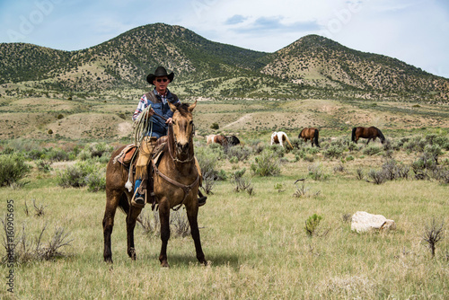 Cowboy wrangler ranch hand with rope on working horse on sage brush prairie