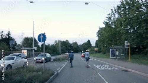 Two skateboarders cross a road and set off. Filmed from behind and dolly. photo