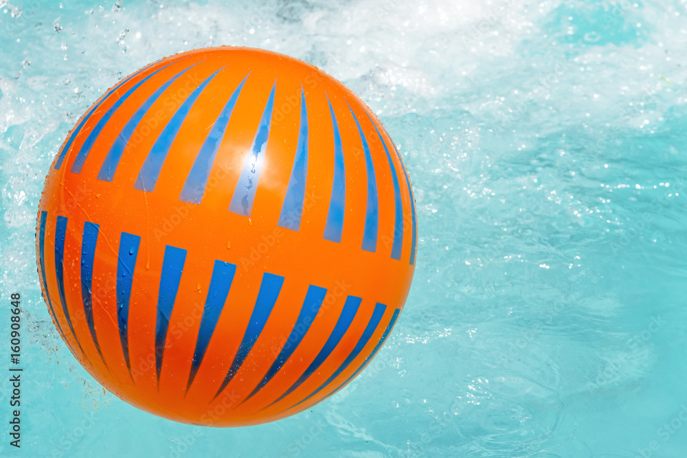 Bright orange and blue beach ball floating in swimming pool Bright orange and blue beach ball floating in swimming pool
