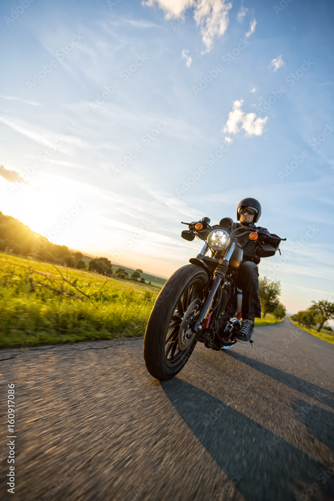 Fototapeta premium Ciemny motocyklista jadący na motocyklu dużej mocy o zachodzie słońca