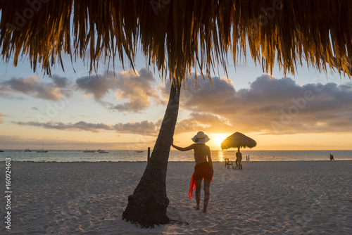 Bavaro Beach, Bavaro, Higuey, Punta Cana, Dominican Republic. Woman by thatch umbrellas on the beach at sunrise (MR). photo