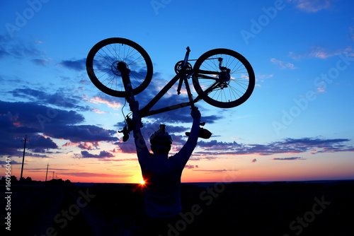 silhouette of a cyclist with arms raised up the bike at sunset.