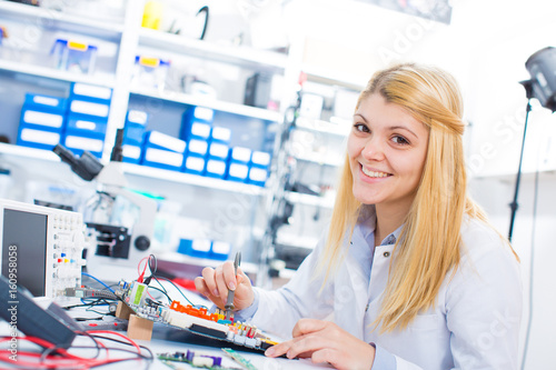 Foto Female laboratory assistant Repairs PCB module for CNC robotics