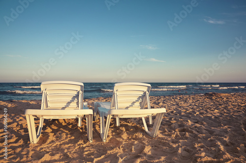 Two deckchairs on the beach with bright sun and waves