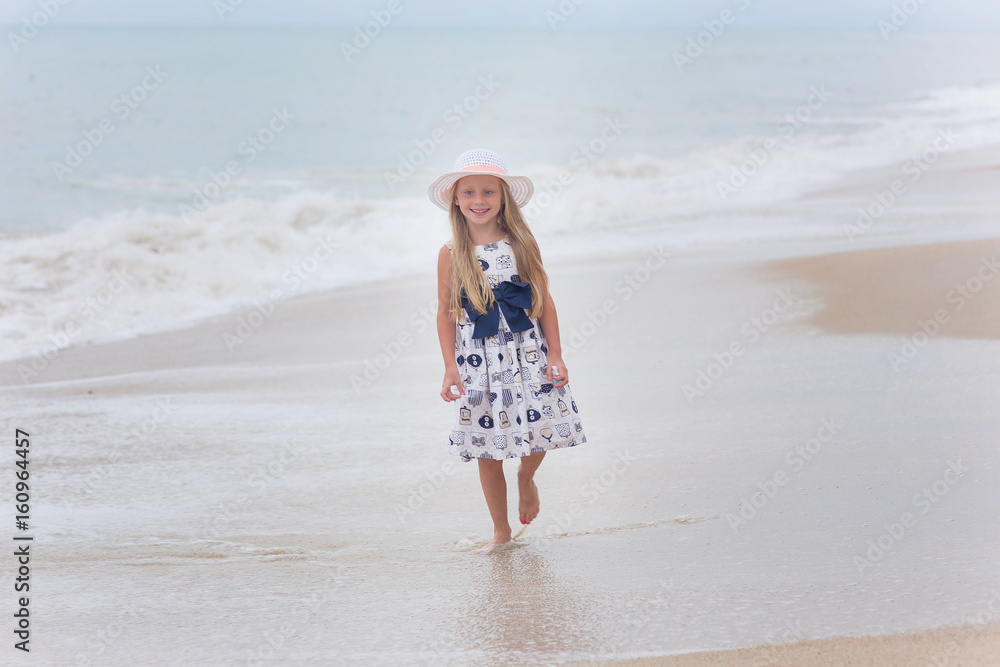 Adorable little girl in hat walking along the shore