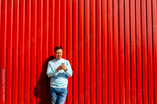 Obraz na plátne Smiling man with smart phone standing on the backgrond of red wall