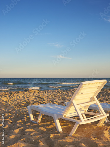Deckchairs on the beach with bright sun and waves © pilat666