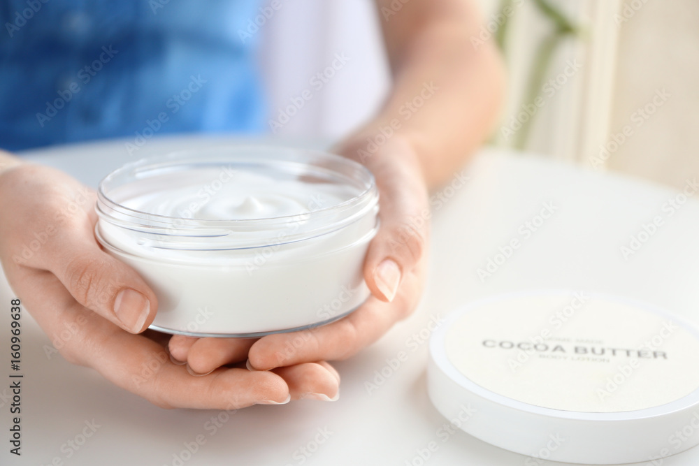 Woman holding jar with cocoa butter lotion over table Woman holding jar with cocoa butter lotion over table
